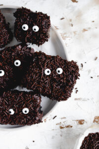 Halloween chocolate brownies with chocolate sprinkles and sugar eyes on a white plate