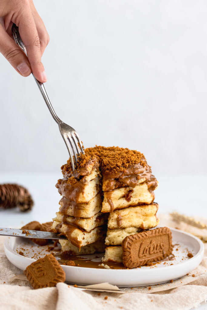 Stack of fully loaded Biscoff pancakes drizzled with Biscoff spread. Sliced with a fork and knife